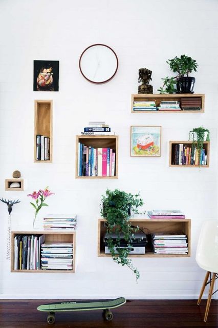 Nichos de madeira, quadrados em parede branca com livros e folhagens em cima.