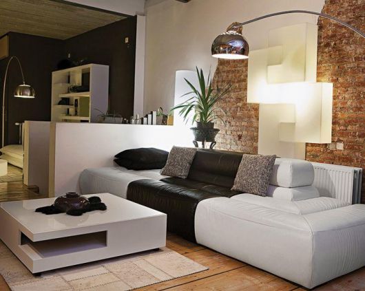 Sala de estar com sofa branco, almofadas pretas e luminaria de chão na cor prata.