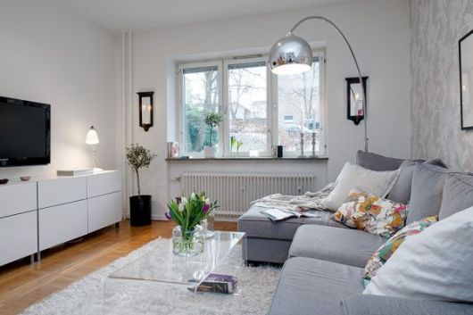 Sala na cor branca com móveis no mesmo tom, com sofá cinza e luminaria prata.
