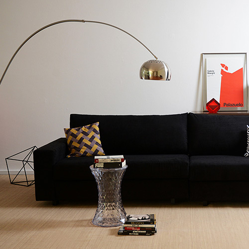 Sala com sofá preto, luminaria dourada.