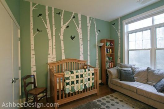 Quarto com piso e móveis de madeira e parede verde com desenho de caules de árvores.