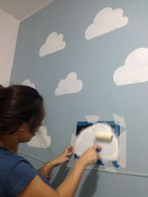 Mulher usando estêncil para fazer nuvens brancas na parede. 