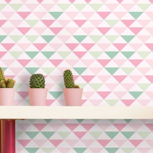 Papel de parede geométrico rosa, verde e branco com prateleira com cactos na frente.