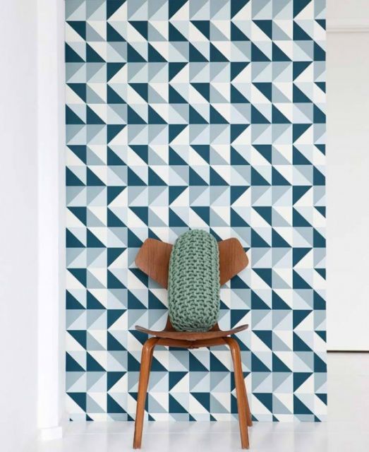 Papel de parede com triângulos brancos, azul claro e escuro, atrás de uma cadeira com almofada.