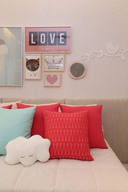 Papel de parede rosa com quadros em cima da cabeceira da cama.