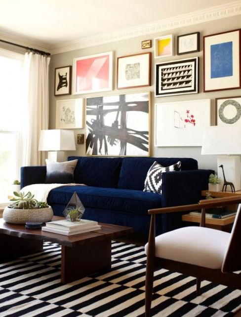 Parede com diversos quadros, com sofá azul encostado.