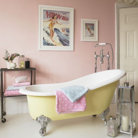 Banheiro pequeno com banheira amarela e paredes em tons rosê.