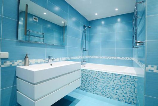 Banheiro na cor azul claro com pia branca e box de vidro transparente.