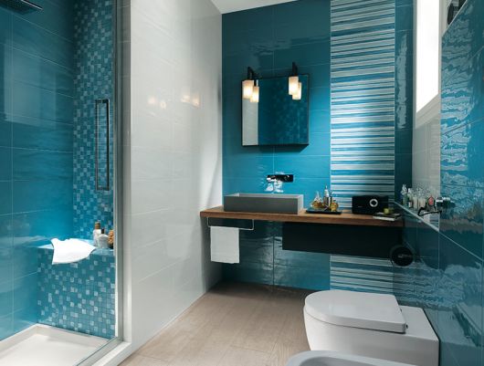 Banheiro pequeno na cor azul escuro com detalhes de adesivos nas cores azul claro nas paredes e pia em madeira na cor marrom.