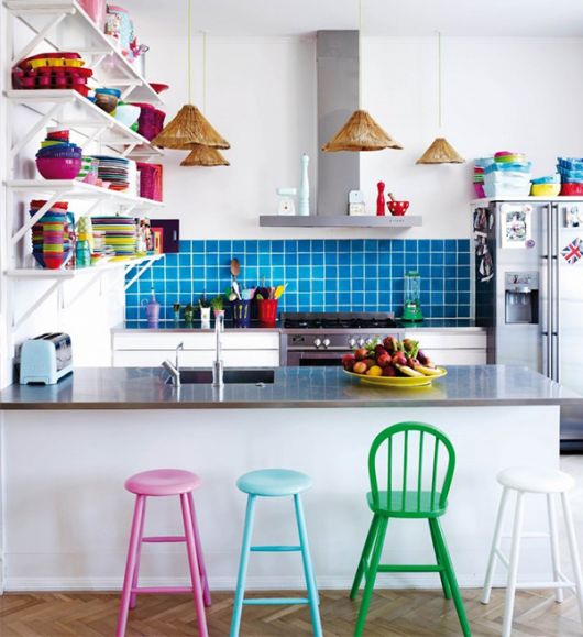 Modelo de cozinha branca com parede de pastilhas azuis e banquetas coloridas.