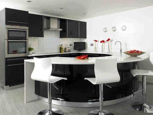 Cozinha preta e branca com balcão oval e cadeiras modernas.