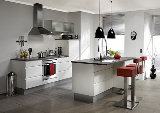 Cozinha branca moderna nas cores branco, cinza e vermelho com banquetas quadradas e balcão estreito.
