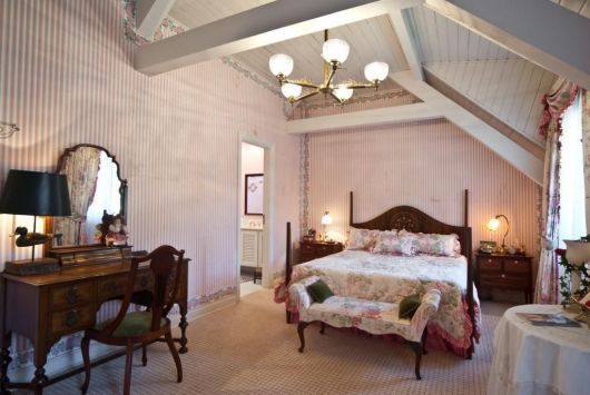 Modelo de quarto clean com cama de madeira rustica marrom, paredes rosa bebê e lustre.