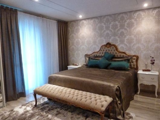 Modelo de quarto com cama de madeira marrom,paredes com papel de parede estampado clean.