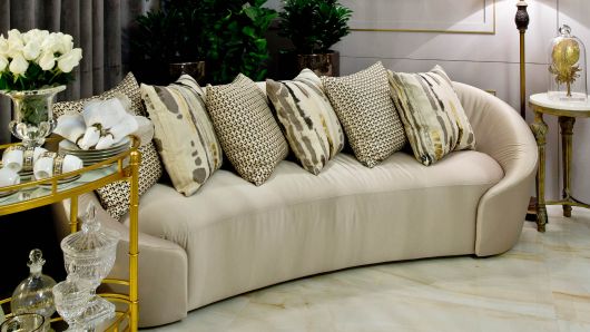 Modelo de carrinho de chá em tons dourados em uma sala com sofá grande em tons de bege.