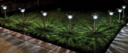 Diversas luminárias solares posicionadas uma ao lado da outra em um jardim durante a noite.