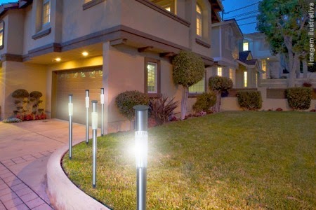 Cinco luminárias solares posicionadas uma ao lao da outra iluminando a entrada do jardim de uma casa grande. 