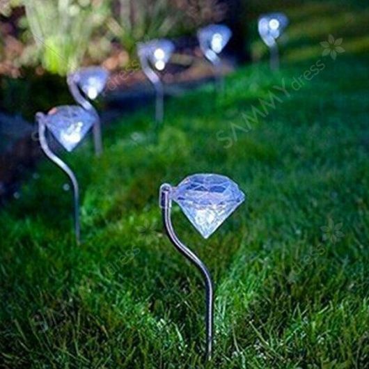 Pequenas luminárias solares posicionadas lado a lado em um jardim com formato de diamante. 