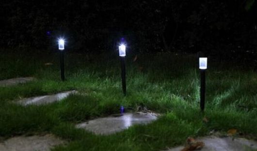 Três luminárias solares instaladas no jardim acesas durante a noite, uma do lado da outra. 