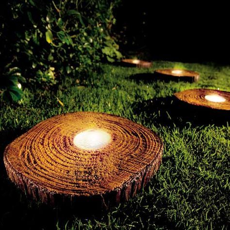Luminárias solares instaladas dentro de tocos de tronco em um jardim próximas umas da outras. 
