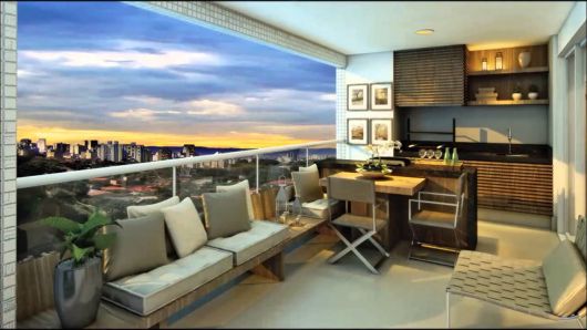 Varanda gourmet grande de apartamento decorada com mesa de jantar, cadeiras e sofá com uma bela vista da cidade durante o crepúsculo. 