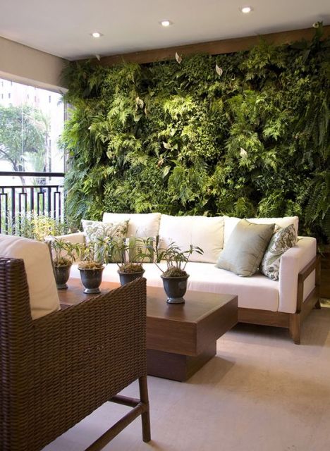 Foto de uma varanda gourmet com sofás e mesa de centro e um jardim vertical bem cheio atrás do sofá. 
