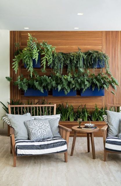 Foto de uma varanda gourmet com duas poltronas e uma parede de madeira ao fundo que comporta um jardim vasos com plantas. 