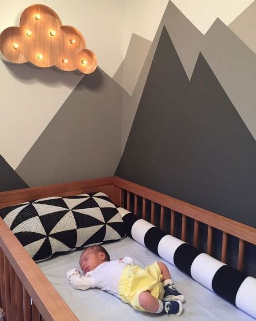 Quarto de bebê com berço de madeira e paredes em branco e cinza.