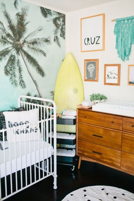 Decoração de quarto de bebê praiana, com prancha de surf e parede com imagem de coqueiros.