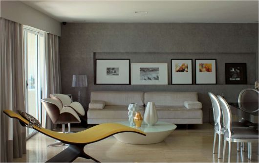 Sala cinza decorada com quadros, sofá branco branco, poltronas, mesa de centro redonda e divã amarelo moderno.