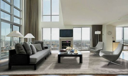 Modelo de sala clean com janelas grandes e sofá cinza.