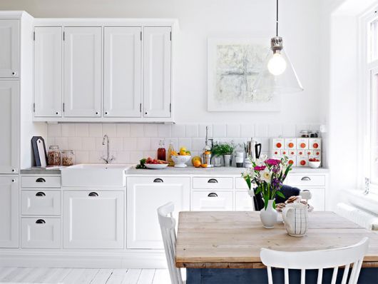 Modelo de cozinha com armários brancos e mesa de madeira estilo mais rústico.