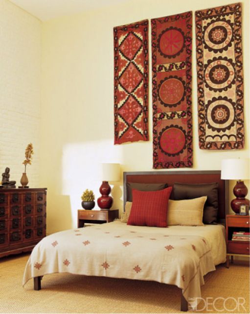 Quarto com decoração amarelo claro nas paredes, tapetes indianos enfeitam a parede acima da cabeceira da cama e a cama combina com toda decoração do quarto indiano.