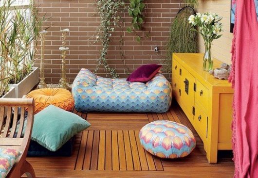 LOcal de meditação com piso de madeira e móvel amarelo, com almofadas coloridas no chão.