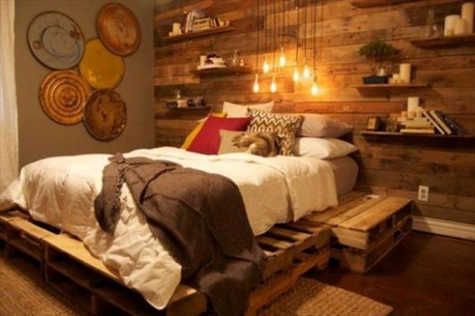 Quarto com cama de madeira de pallets, decoração em tons de marrom, branco e amarelinho claro.