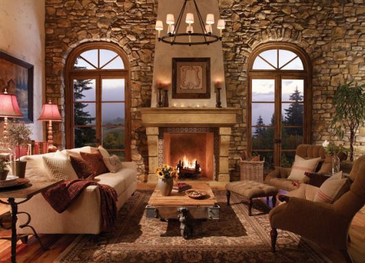 Sala rústica com paredes de pedras, lareira, sofá e tapeçaria em estilo rústico.