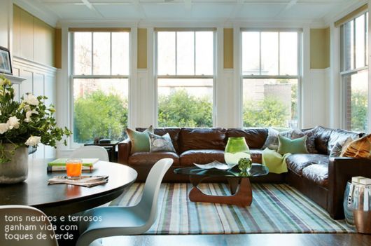 Sala iluminada com sofá marrom grande e fofo, janelas grandes e mesa de centro de madeira.