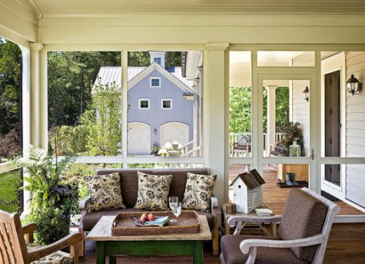 Varranda fechada com sofá marrom clássico, almofadas estampa floral e janelas grandes.