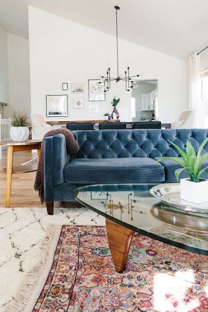 Sala ampla clean com paredes brancas, quadros pequenos mesa de centro de vidro e sofá azul.