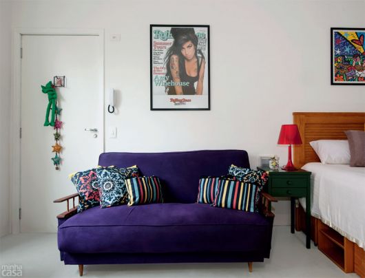 Sala clean com quadro da cantora Amy, sofá azul com almofadas estampadas.