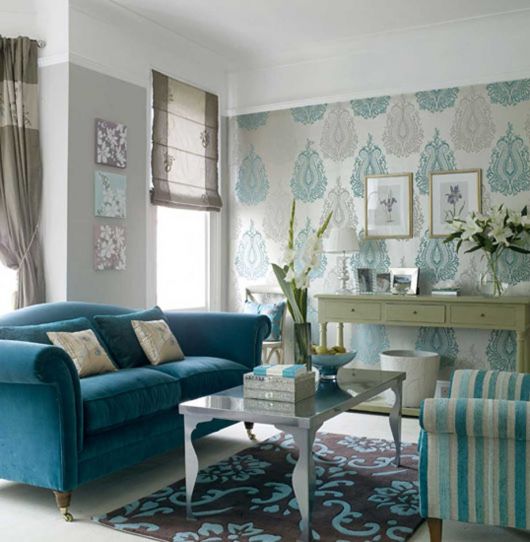 Modelo de sala com papel de parede estampado sutil, mesa de centro cinza e sofá azul escuro com almofadas de cores mescladas entre nude e azul marinho.