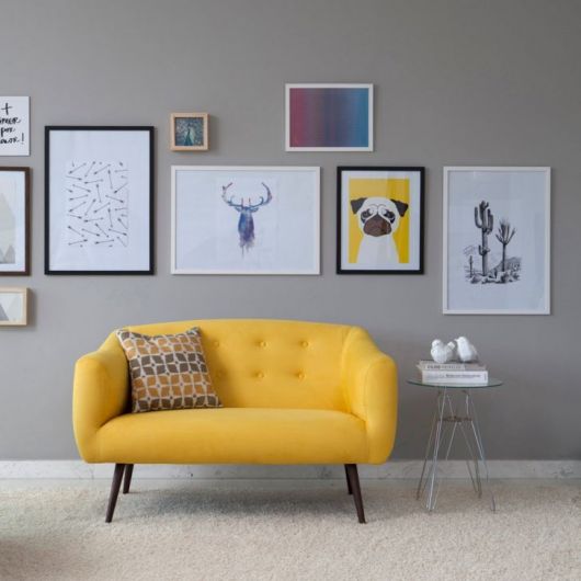 Sala cinza com sofá na cor amarela com quadros de desenhos diversos.