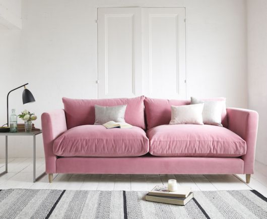 Sala branca com tapete estampado em cinza e sofá cor de rosa.