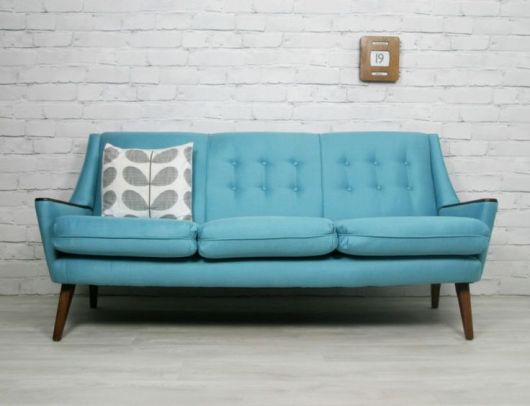 Sala com paredes de tijolo a vista na cor cinza com sofá azul de três lugares.