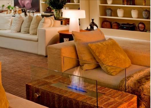 Foto de uma lareira ecológica entre dois sofás com as chamas protegidas por dois vidros laterais. 