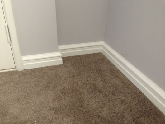Rodapé de gesso na parte inferior de uma parede com o chão coberto por carpete. 