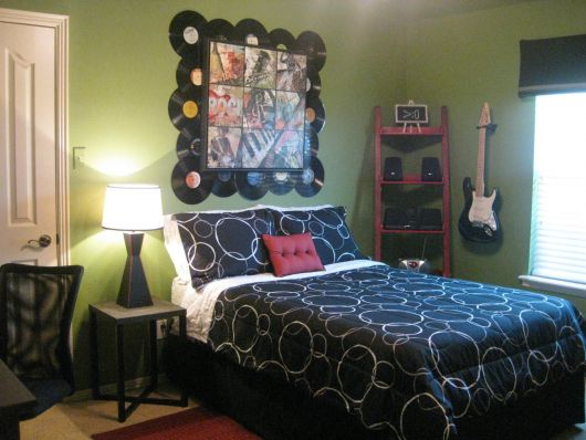 Quarto com um quadro acima da cama cuja moldura é feita de discos de vinil e na parede lateral há uma guitarra pendurada. 