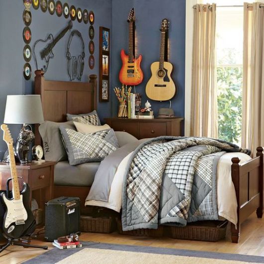 Foto de um quarto com uma guitarra e uma caixa de som posicionadas ao lado da cama. Acima dela, há diversos discos de vinil pendurados e uma guitarra elétrica ao lado de um violão, ambos também pendurados. 