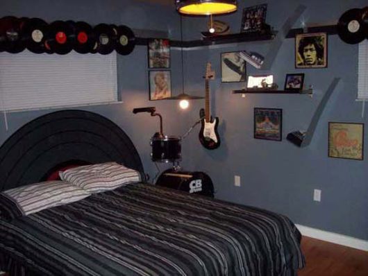 Foto de um quarto com a cabeceira da cama similar a um disco de vinil. Na parede há diversos discos de vinil, instrumentos musicais e quadros de ícones do rock.