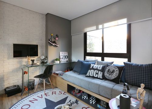 Sala de estar com um sofá repleto de almofadas que fazem referências ao rock e um tapete da All Star Converse. 
